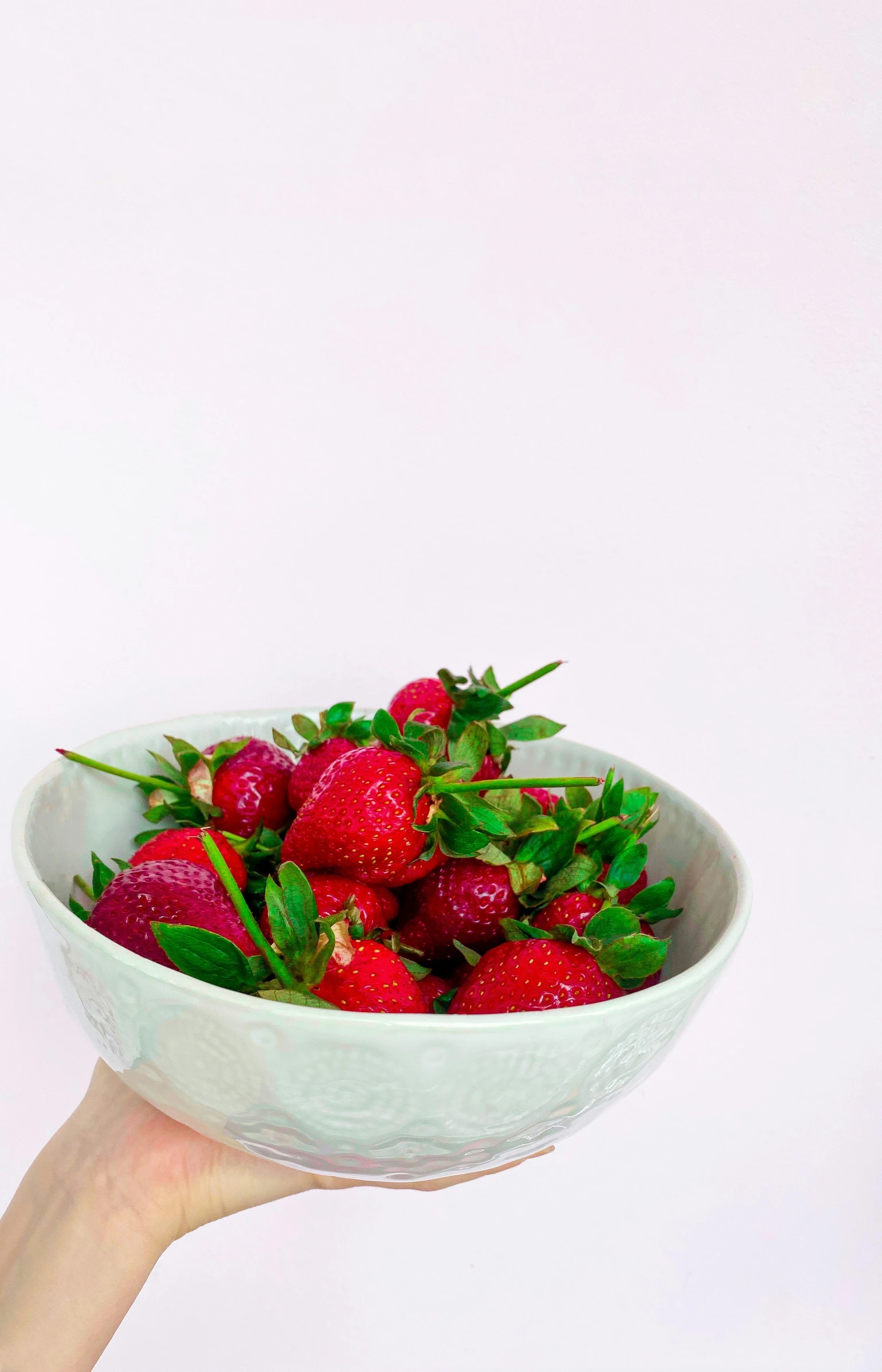 a person holds a bowl of strawberries up into the air