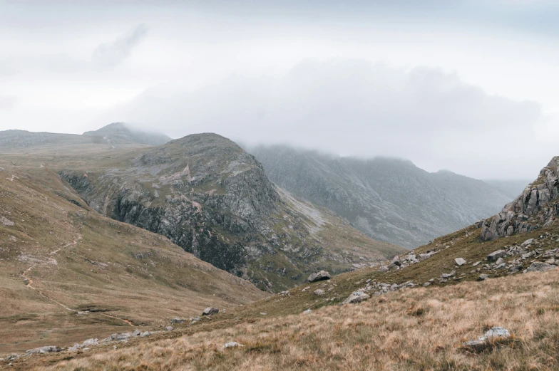 grassy hills covered in grey mountains under cloudy skies