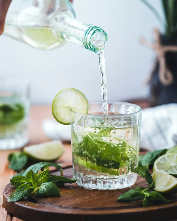 a green drink being poured into a glass with ice and mint on the side