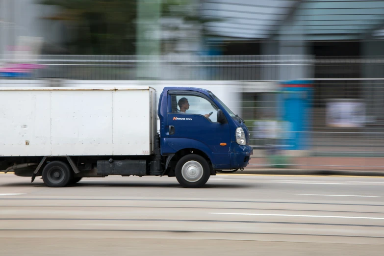 a small blue truck drives down a street