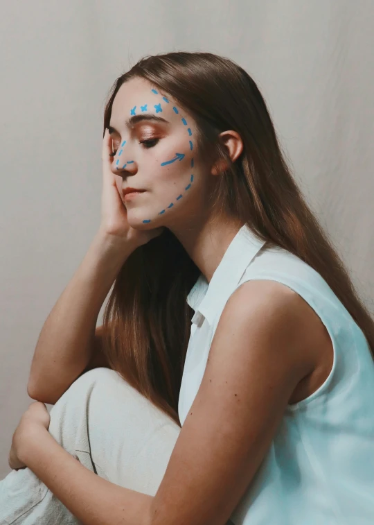 a girl with pix blue dots on her face and shoulder, covering her face