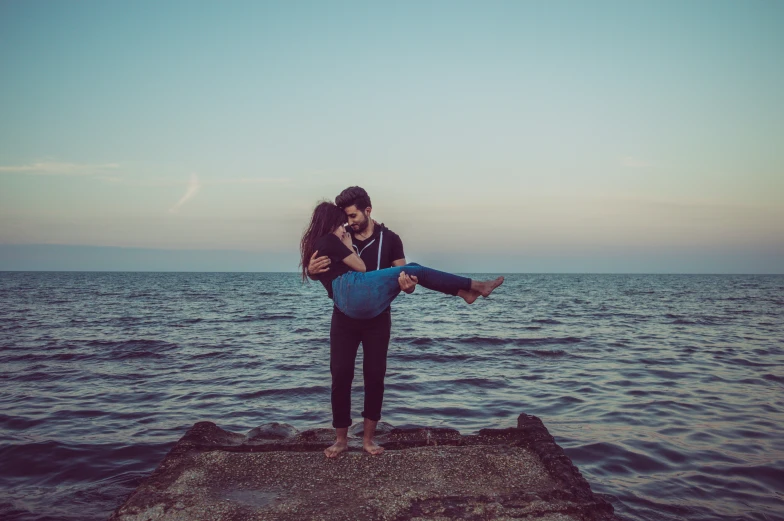 man is lifting woman into the air over water