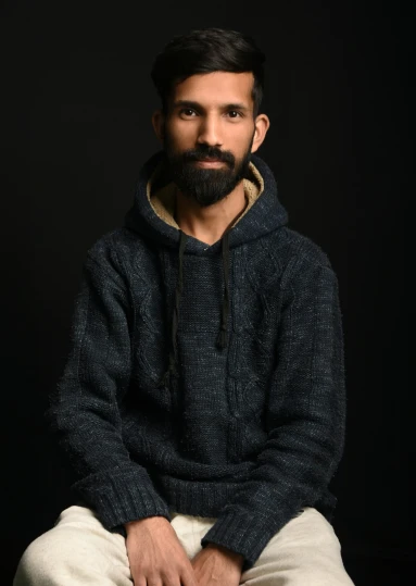 a man sitting down with a beard and wearing a sweater