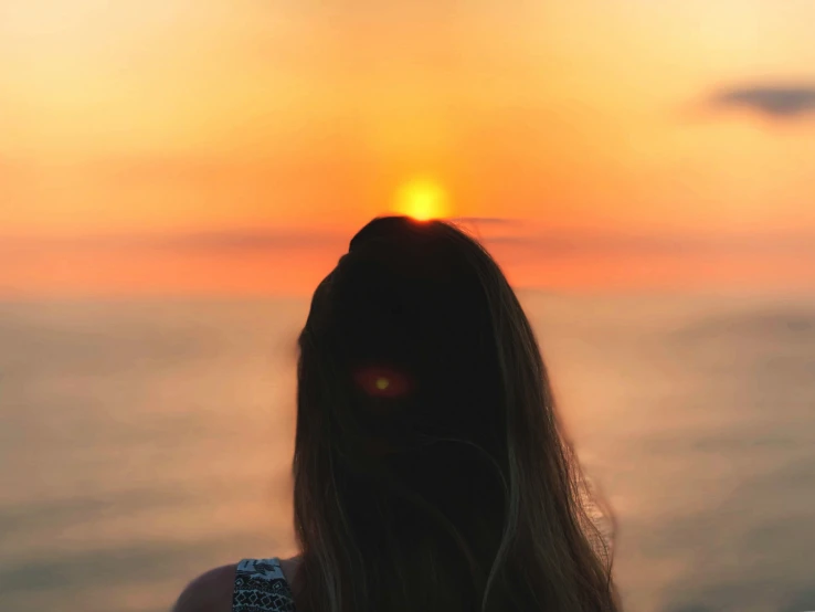 a woman with long hair standing in front of the sun