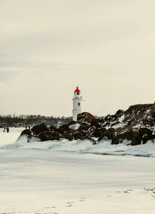 people walking on the snow near a snowy lighthouse