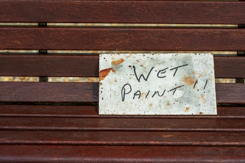 a white, dirty sign that says wet paint on a park bench