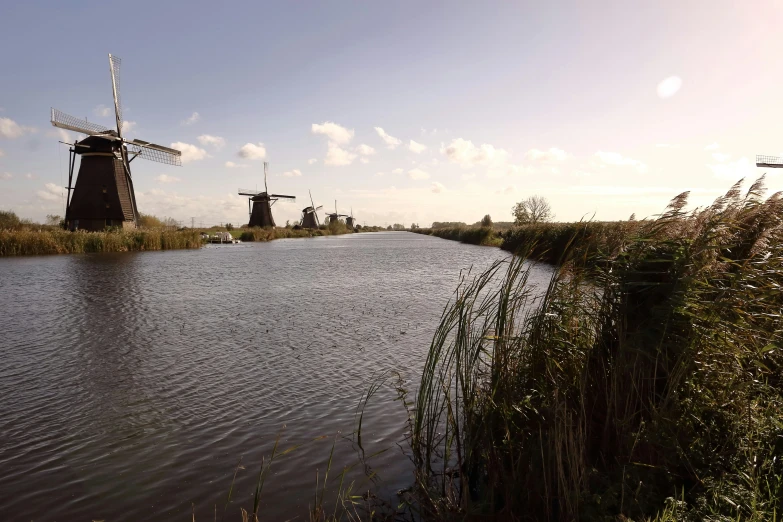 a body of water next to tall, brown windmills