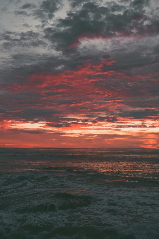 a red sky with the sun rising over a rocky coast