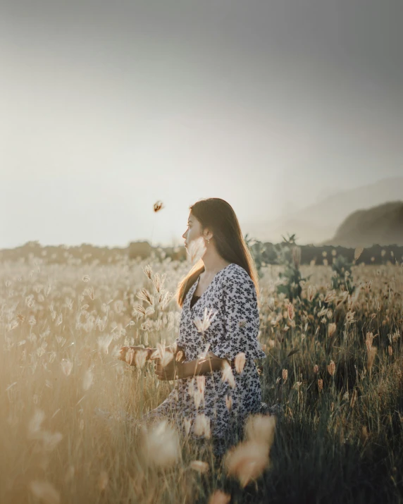 the young woman is sitting in the field blowing in the wind