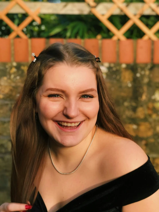 smiling young woman in black off shoulder top standing next to wall