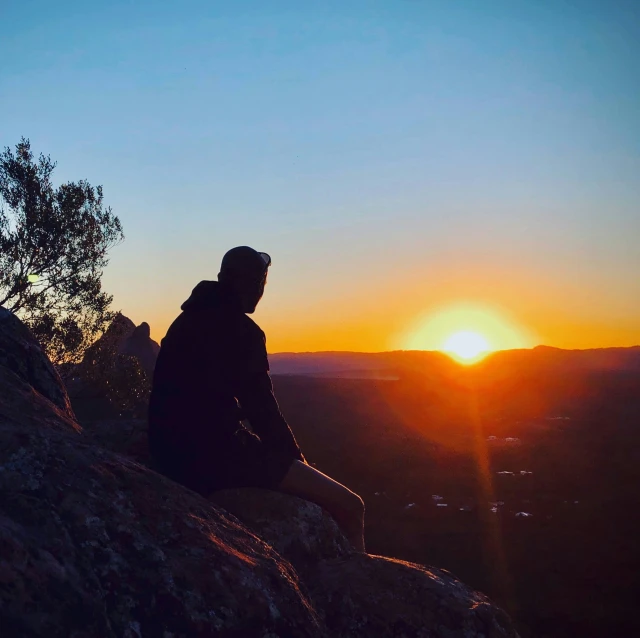 a person sits on top of a rock near the sun