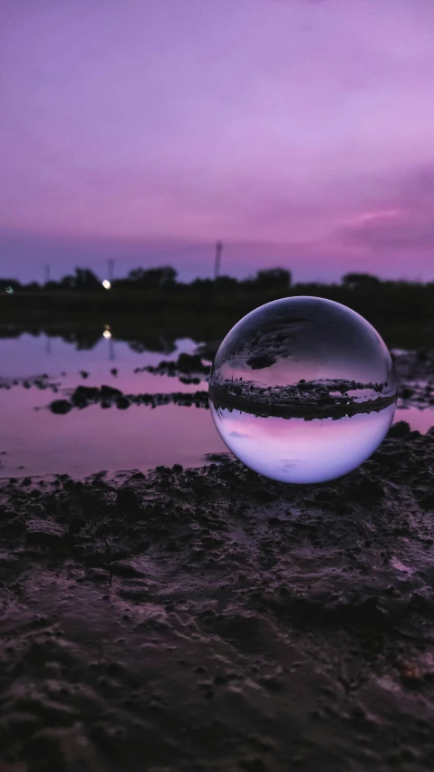 a large sphere is on the sand in front of a river