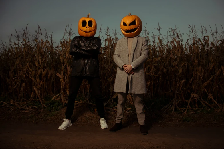 two people stand with pumpkin faces in a cornfield