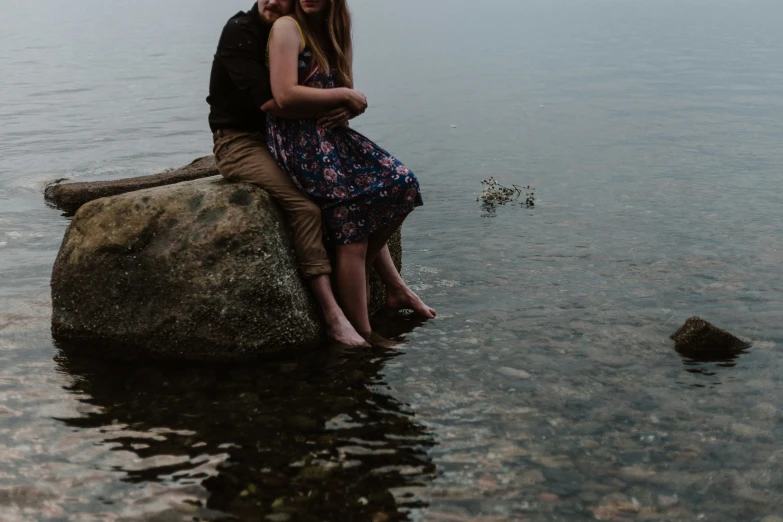 a man and woman sit on a large rock in the water