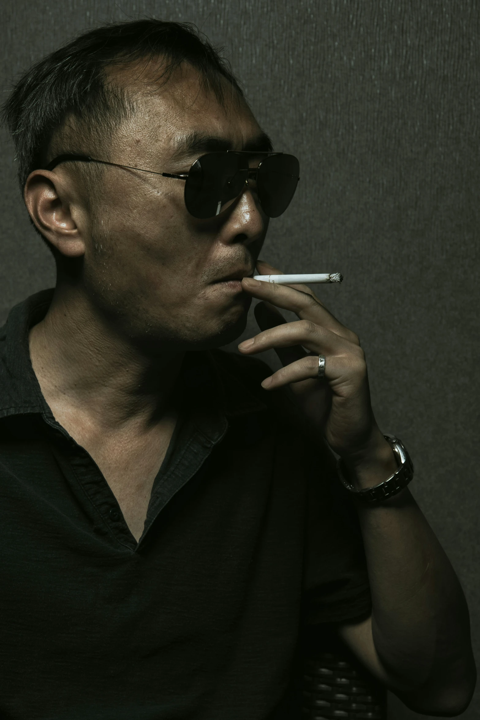 man with sunglasses smoking a cigarette in front of a grey background