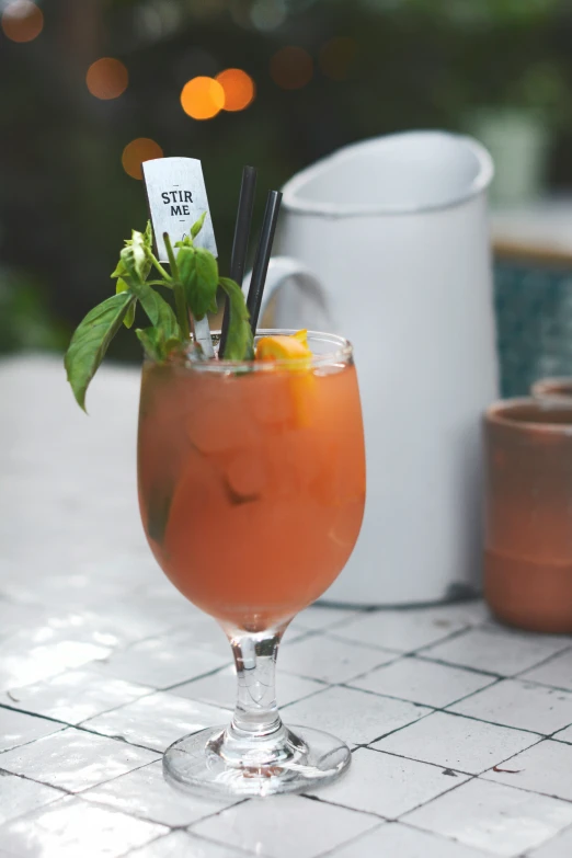 an alcoholic cocktail with garnish sits on a tile table