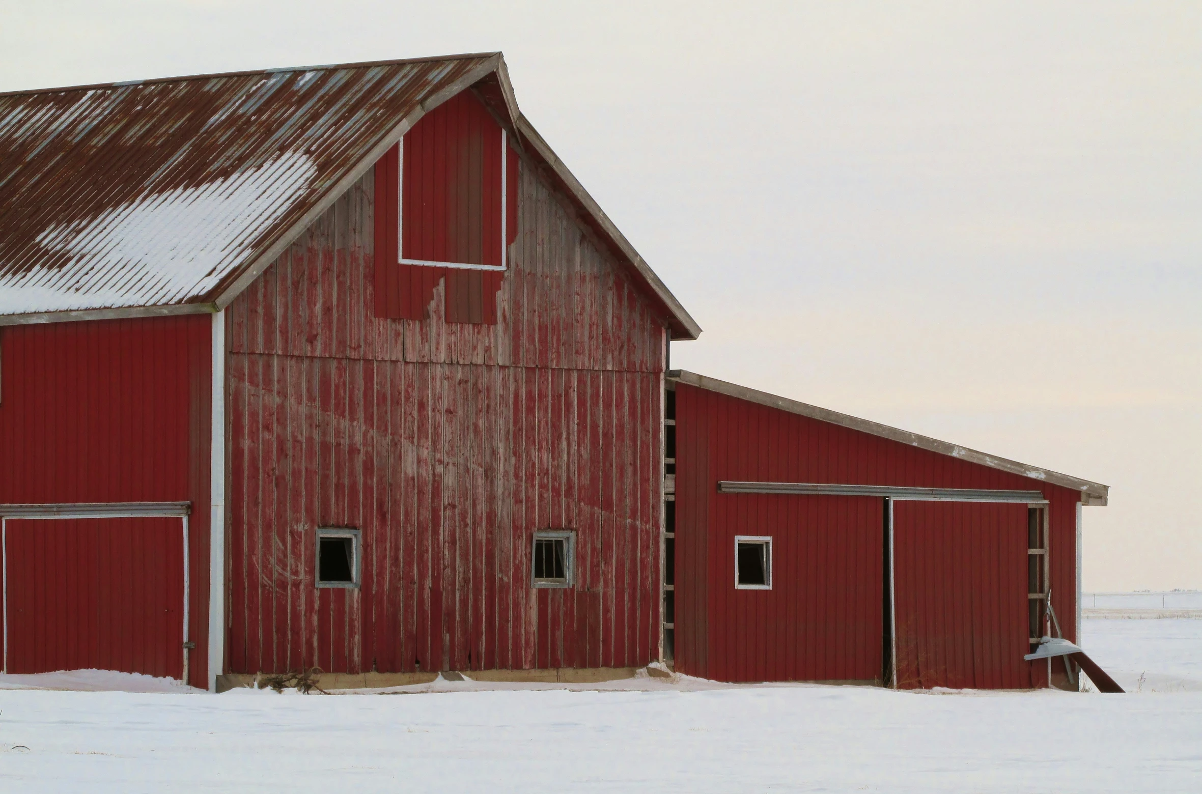 a red barn with two large windows on it in the snow