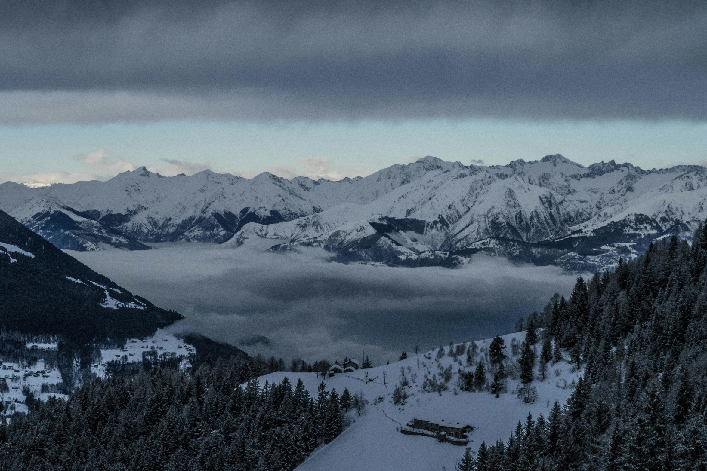 a snow covered mountain scene with clouds and a bench