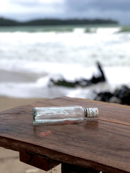 an empty glass bottle is sitting on a wooden bench