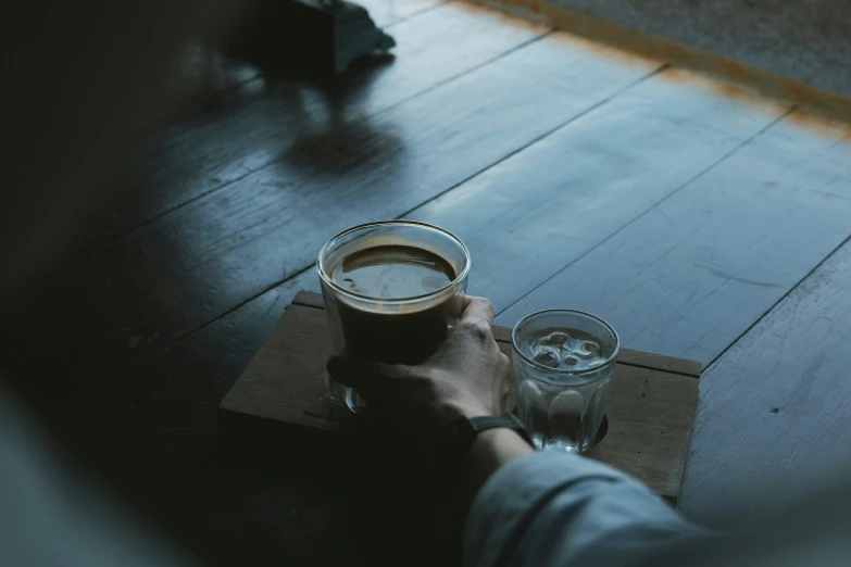 a person holding a drink glass on top of a wooden floor