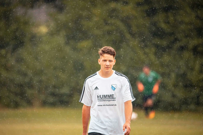 young man playing in the rain with a soccer ball