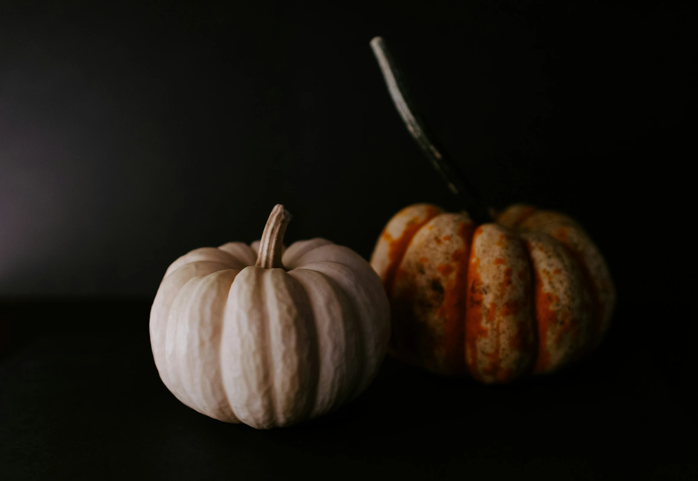 two pumpkins sitting side by side in dark room