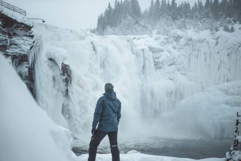 man in front of a waterfall with snow on it