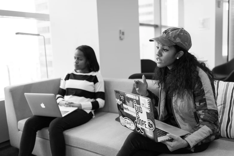 two girls sitting on a couch with laptops in front of them