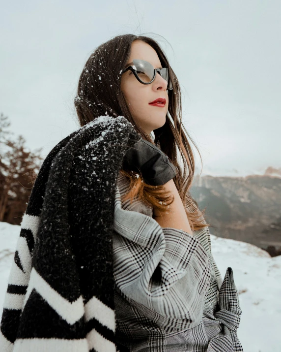 a girl standing in the snow wearing a plaid coat