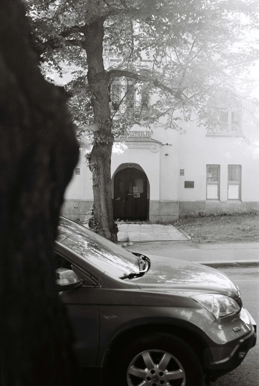 a small old building near a tree and a car