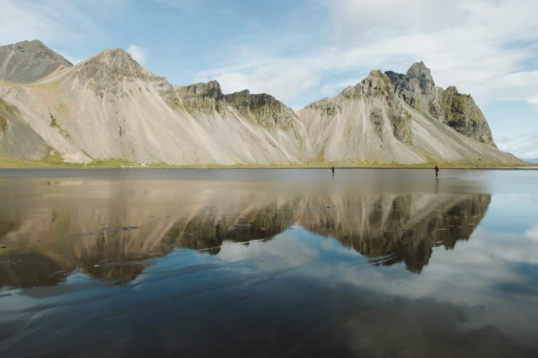 two people walking through the mountains next to a lake