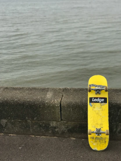 a yellow skateboard resting on the concrete wall of a walkway by the water