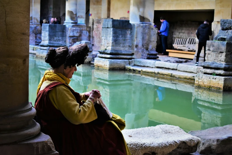 a woman sitting on the ledge next to a pond