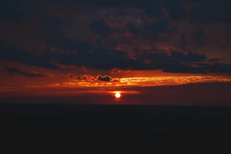 the sunset is lit by a cloudy sky over the ocean