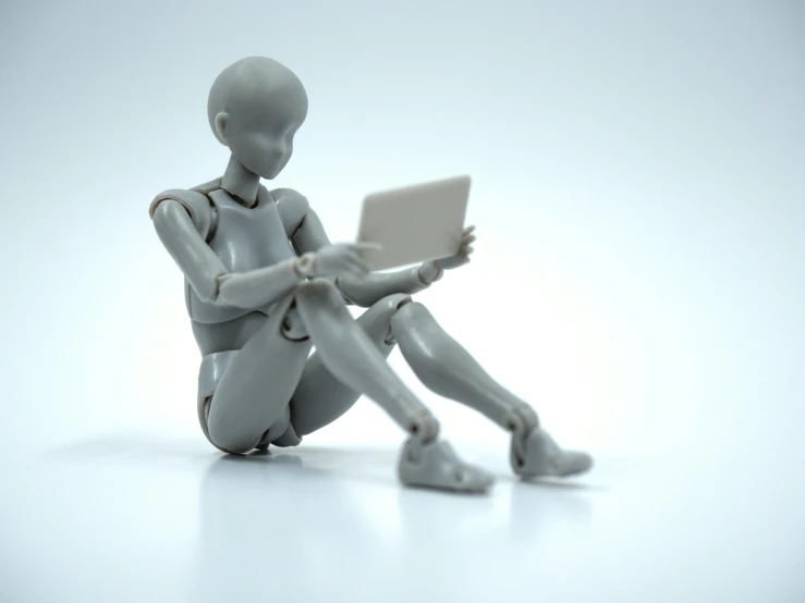 an artificial person sits on the ground working on a laptop