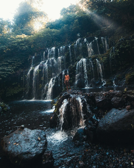a man is standing in the water near a waterfall