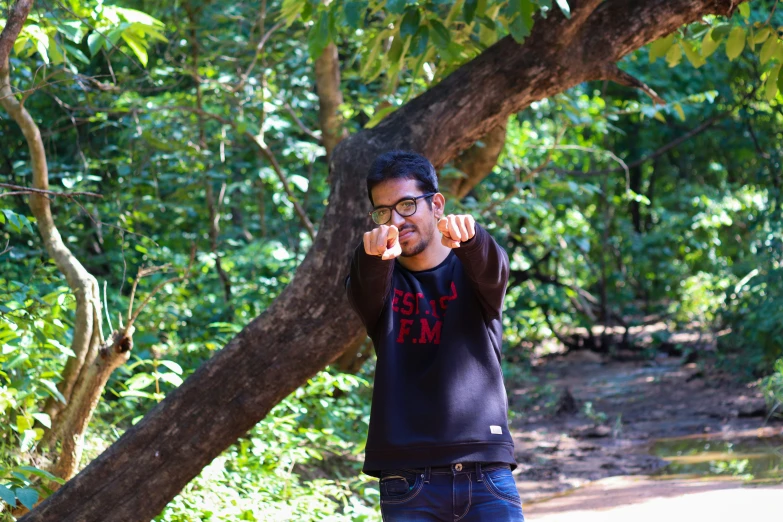 a man pointing to the camera, leaning on a tree