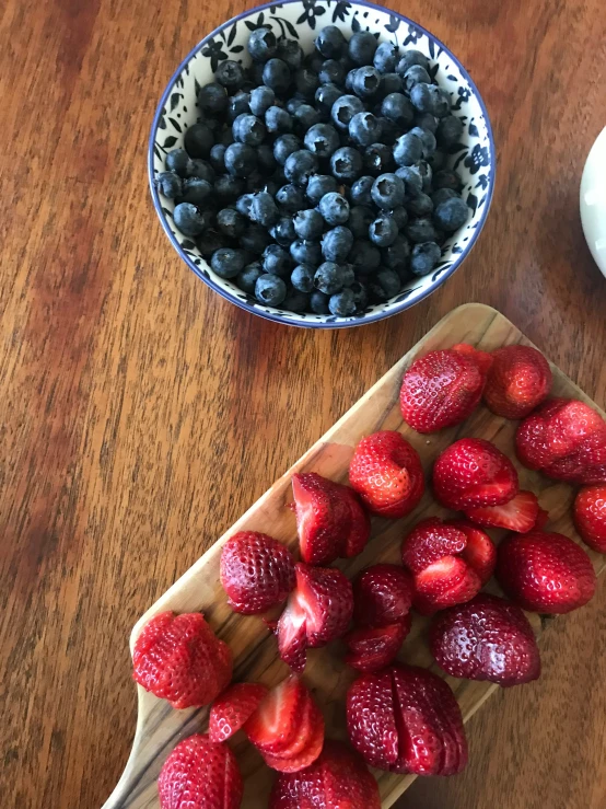strawberries and blueberries are arranged in bowls on the table