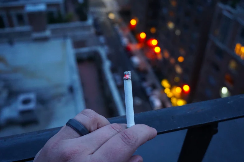 someone holding a cigarette in their hand over a ledge