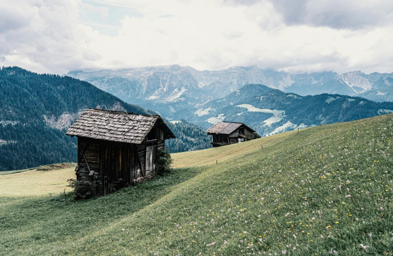 wooden structures in grassy field with mountains in background