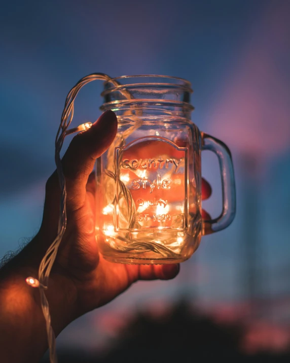 a person holding onto a lit up mason jar