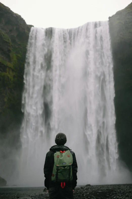 the man is in front of the waterfall looking at the water