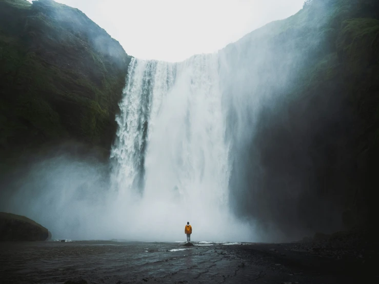 a man stands near a waterfall while looking up at it