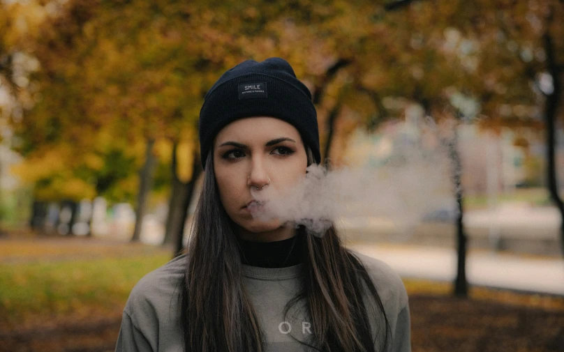 a woman with a knit hat on, smoking a cigarette in the street
