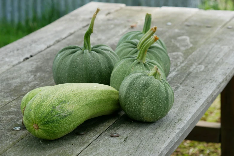 three green fruits sitting on top of a wooden picnic table