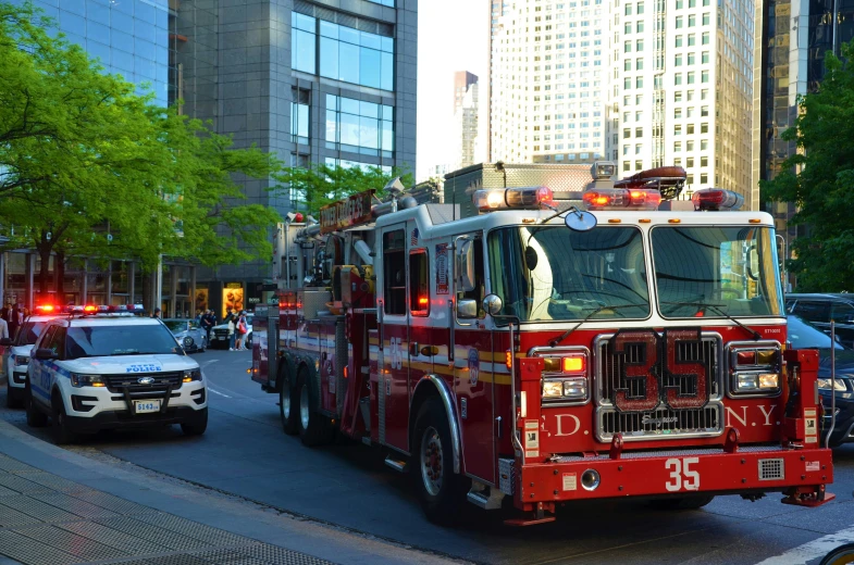 two fire trucks, one with flashing lights, driving down the road