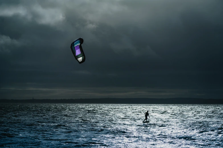 a man standing in the water holding onto a parachute with the sky and ground covered by dark clouds