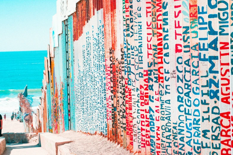 the colorful wall of words covers a path leading to the ocean