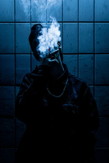 man smoking in the dark with blue tiled background