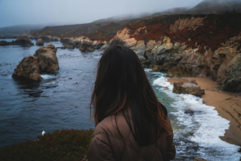 a woman standing on a cliff looking at the ocean